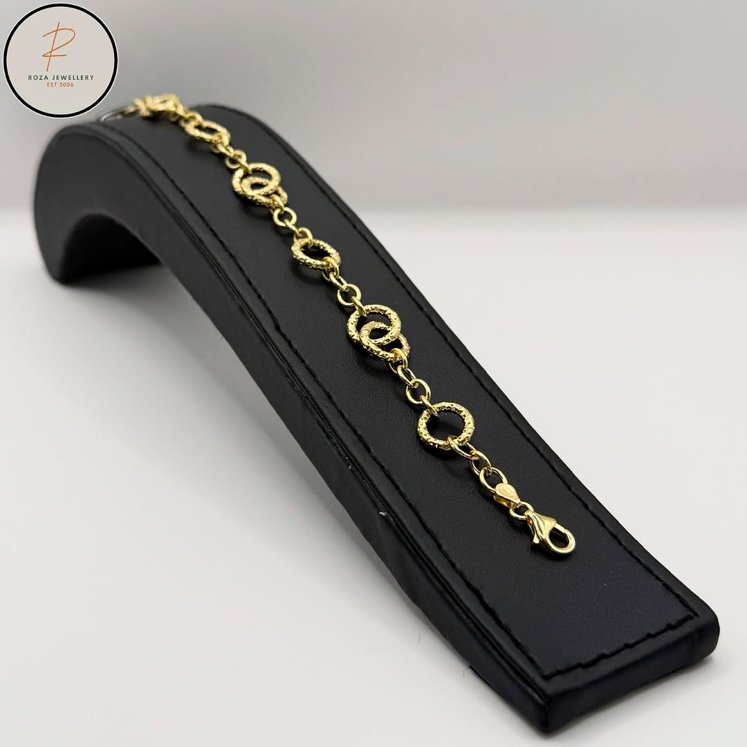 Textured gold circle-link bracelet displayed on a black stand
