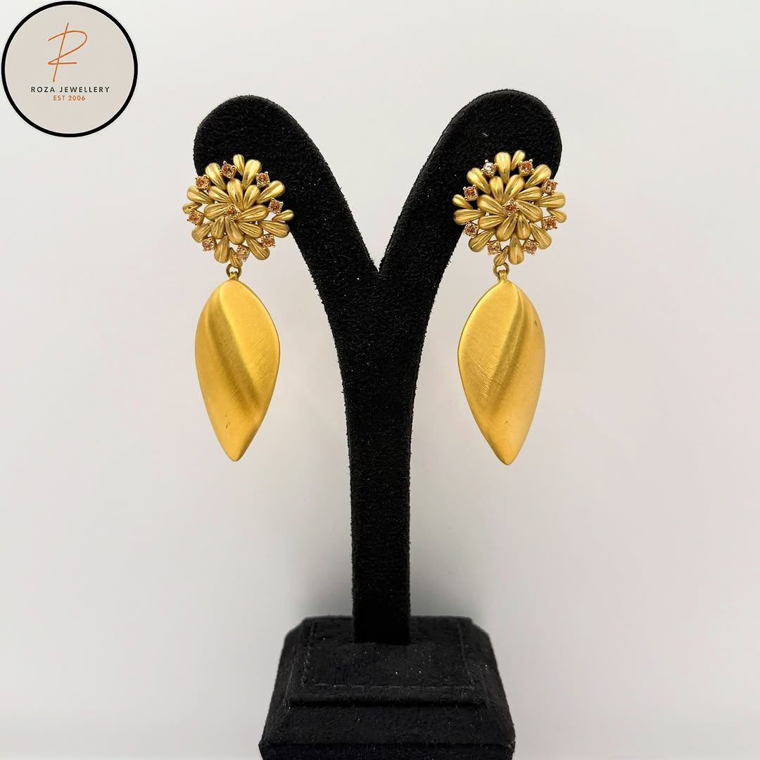 Gold floral drop earrings displayed on a black stand
