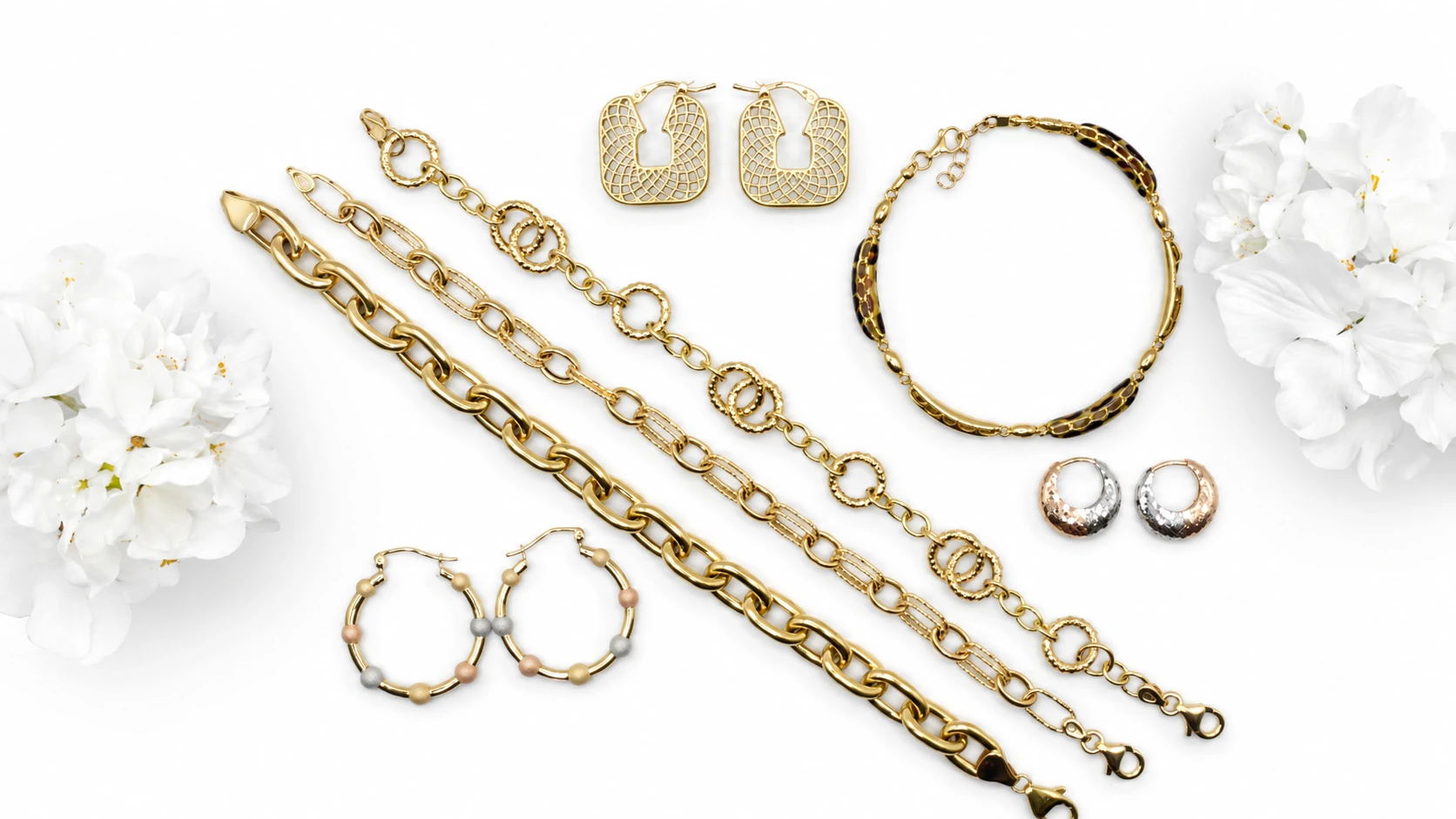 Assorted gold bracelets, necklaces and earrings arranged with white flowers